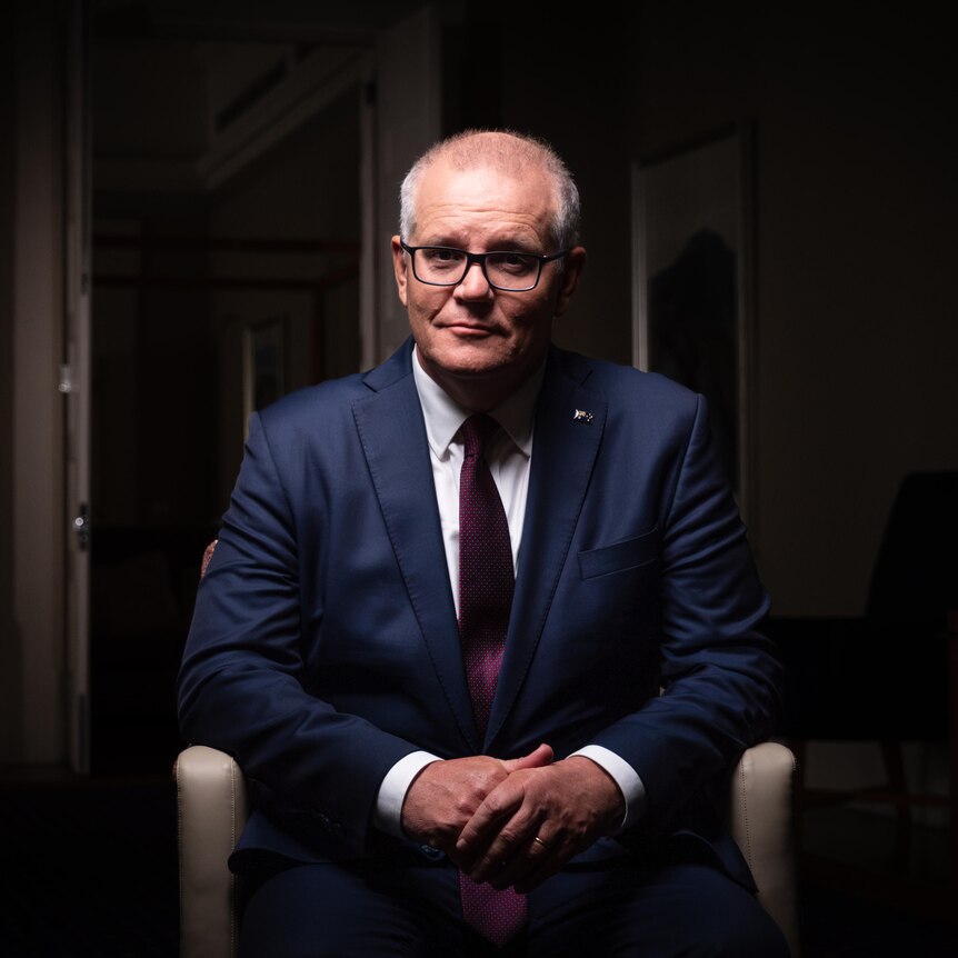 Dressed in a suit and tie, Scott Morrison sits in a chair, looking into camera with a serious expression.