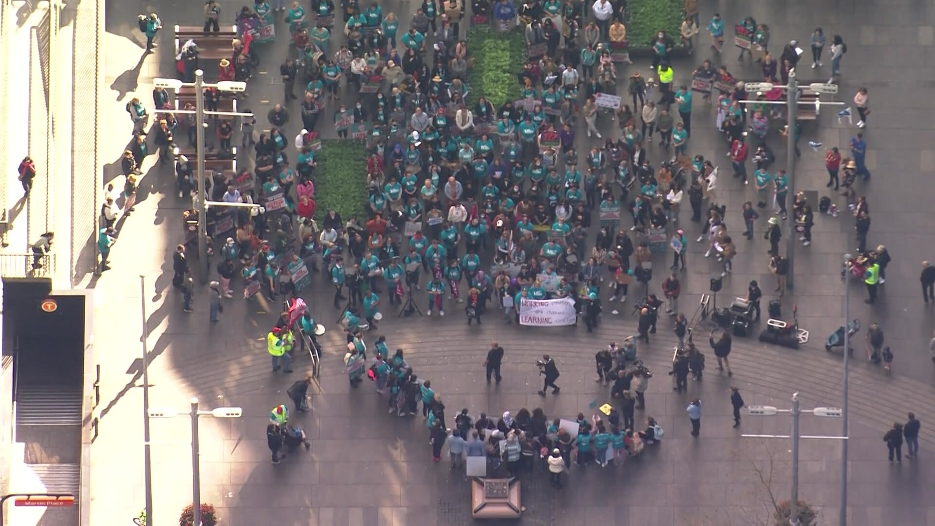 Hundreds of people wearing light green shirts and holding signs gather in the city of Sydney.