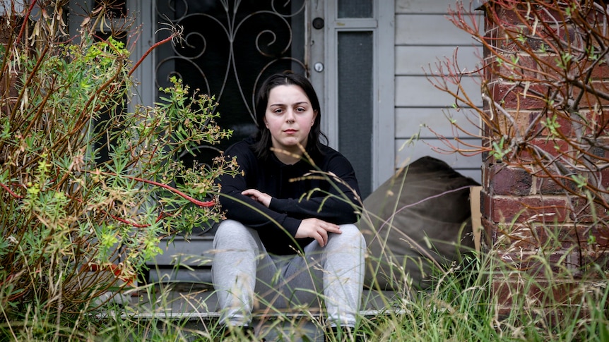 A woman sits on the front step of a house looking at the camera