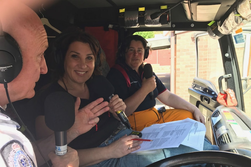 Gorr, Lapsley and Clothier sitting in front seat of fire truck with headphones on and holding microphones.