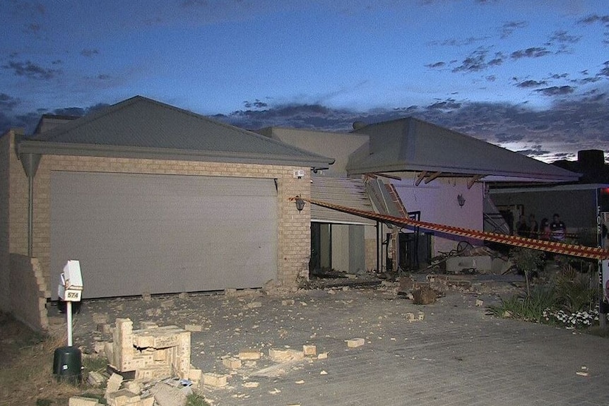 A house with broken walls and bricks strewn across its front yard.