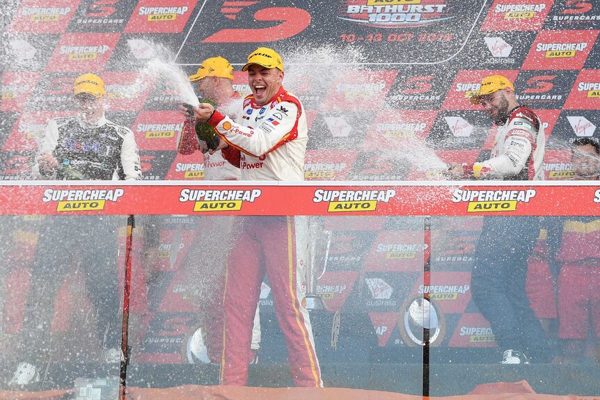 A SuperCars driver smiles as he sprays champagne over the crowd following his Bathurst 1000 win.