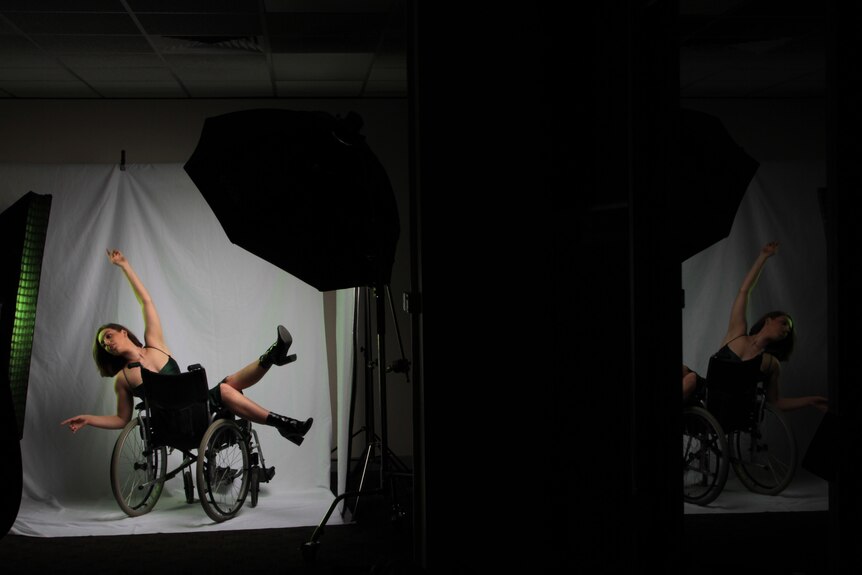 A person laying across a wheelchair models in front of a backdrop
