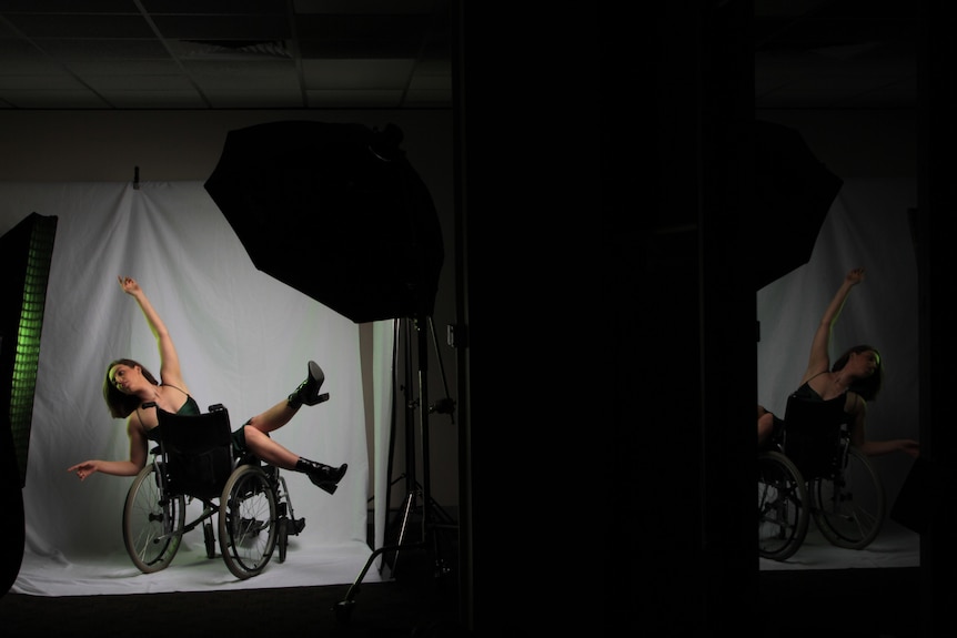 Une personne allongée sur un fauteuil roulant modélise devant une toile de fond