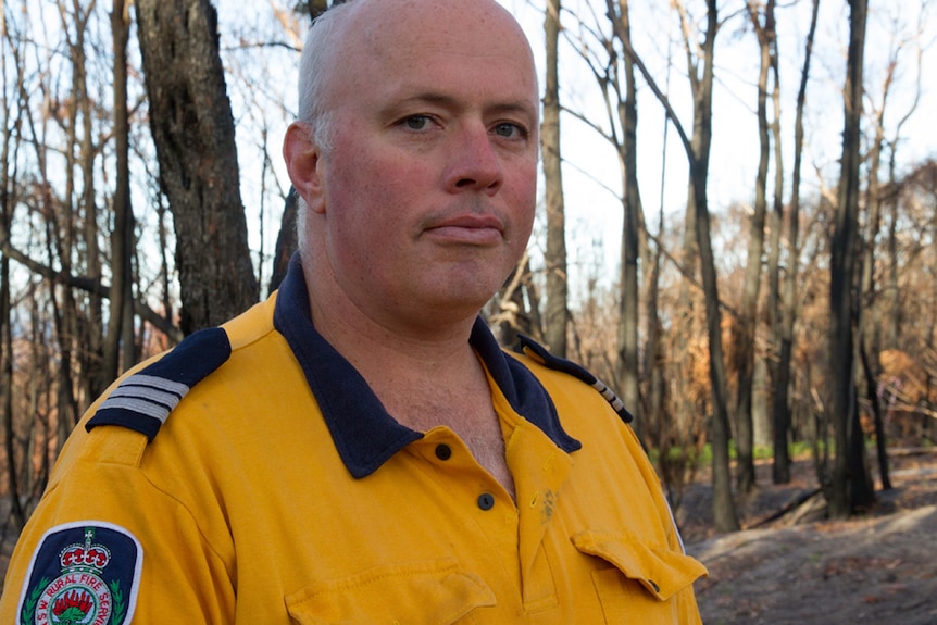 Portrait photo of Tathra RFS Captain Adam Wiggins standing in burnt out bushland