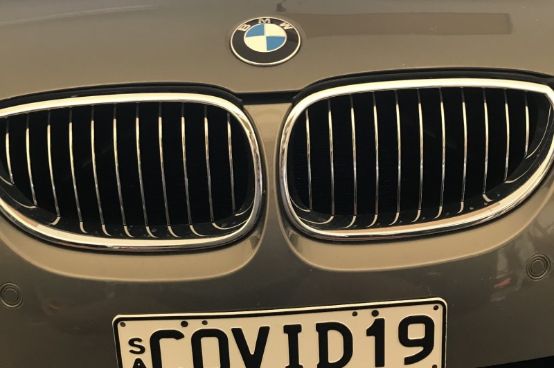 A silver car grill with a bmw logo. The licence plate shows the word COVID19.