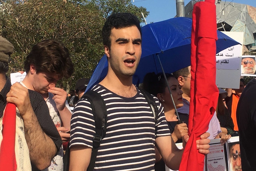 Damoon standing at a protest wearing a black and white striped shirt