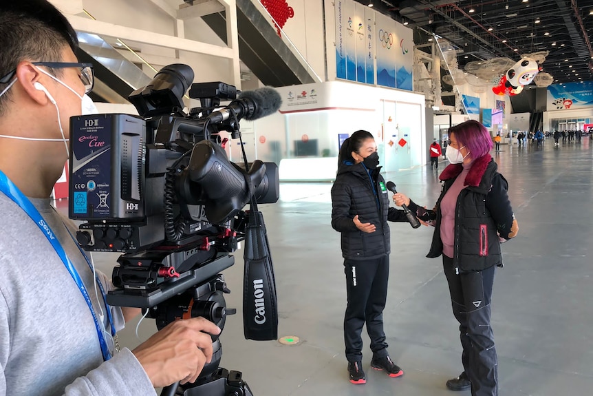 A female presenter interviews a femaile athlete while the video cameraman can be seen filming to the left of picture.