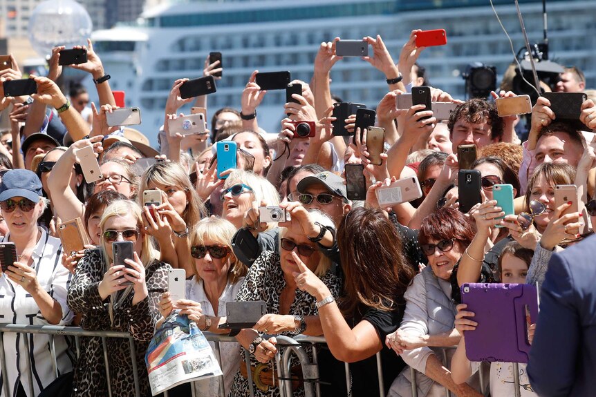 A crowd of people outside the Sydney Opera House with their phones ready to take pictures of the royal couple.