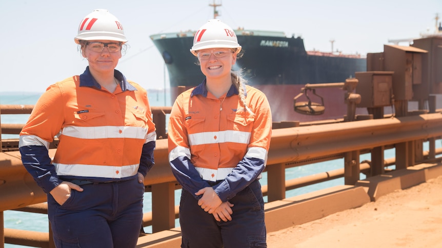 Two young women wearing orange high vis and hard hats standing in front of large vessel