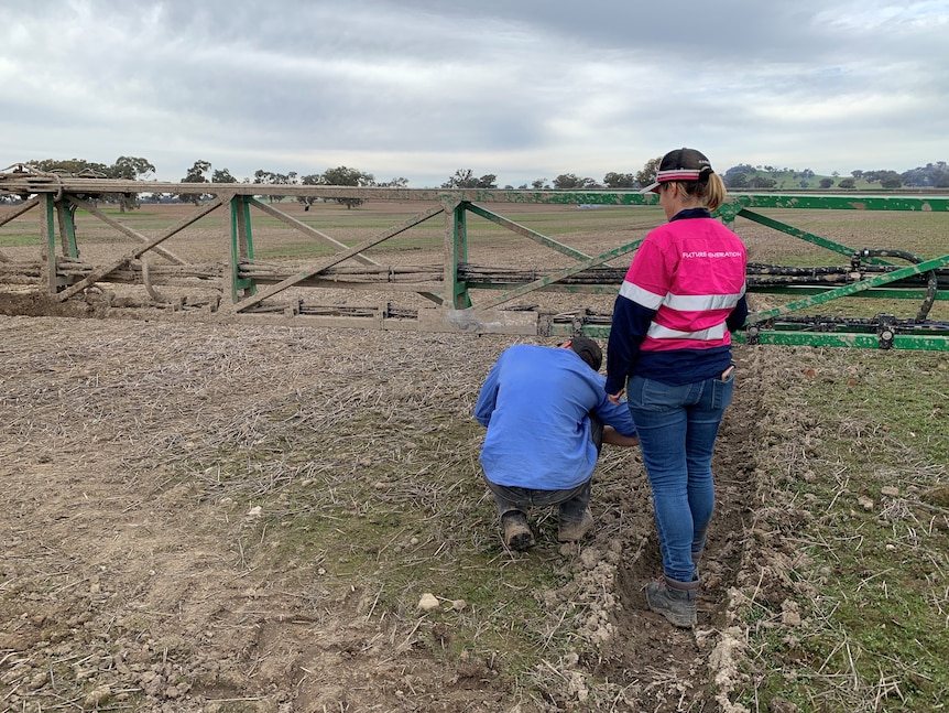 A man and woman looking a green spray boom that is covered in mud. 