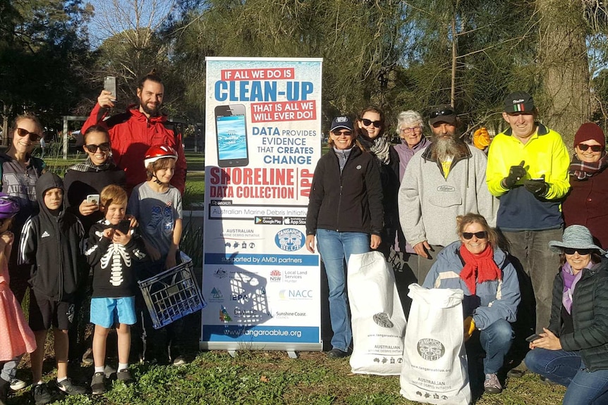 A group of people including children gather around a sign in a park.