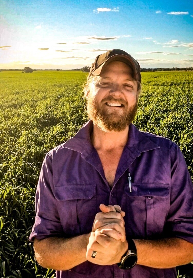 A man with a beard standing in front of some crops