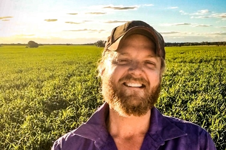 A man with a beard standing in front of some crops