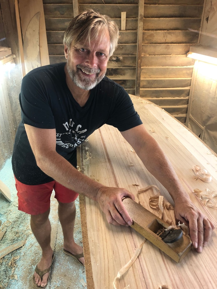 Tom Wegener sands down a wooden surfboard.