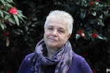 A woman with short grey hair and a grey scarf looking into the camera