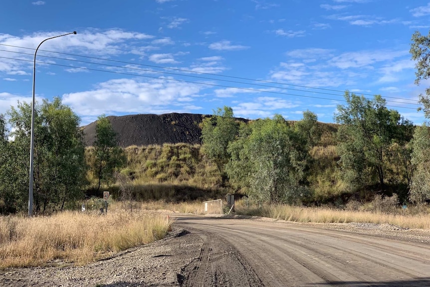 A dirt track leads through a gate and towards a coal mine. There are powerlines and a light post over the road