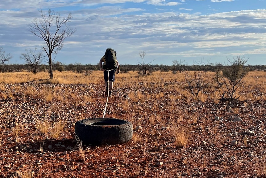 A man in a rocky landscape pulling a tyre with a back pack on