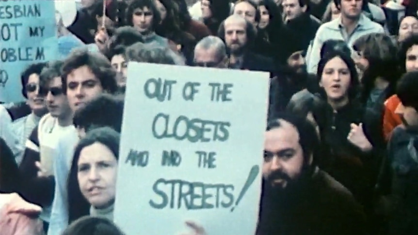 A protest crowd, protest sign reads: "Out of the closets and into the streets!"
