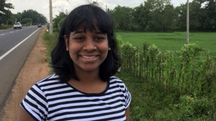 A young woman smiles as she stands by a road and farmland