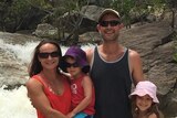 Family of four standing together in front of small waterfall