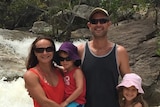 Family of four standing together in front of small waterfall