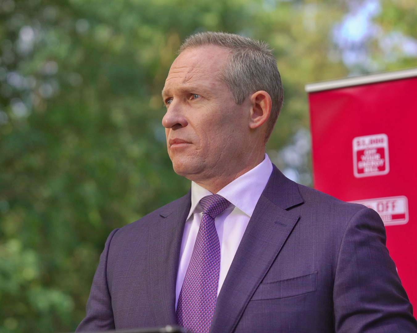 A man in a suit at apress conference looking to the left.
