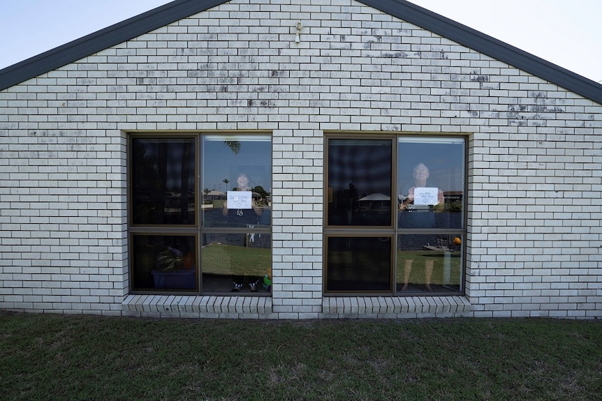 A man and a woman stand at the window of their home holding signs