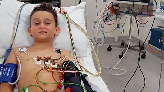 Boy lays in a hospital bed attached to machines and monitors.