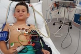 Boy lays in a hospital bed attached to machines and monitors.