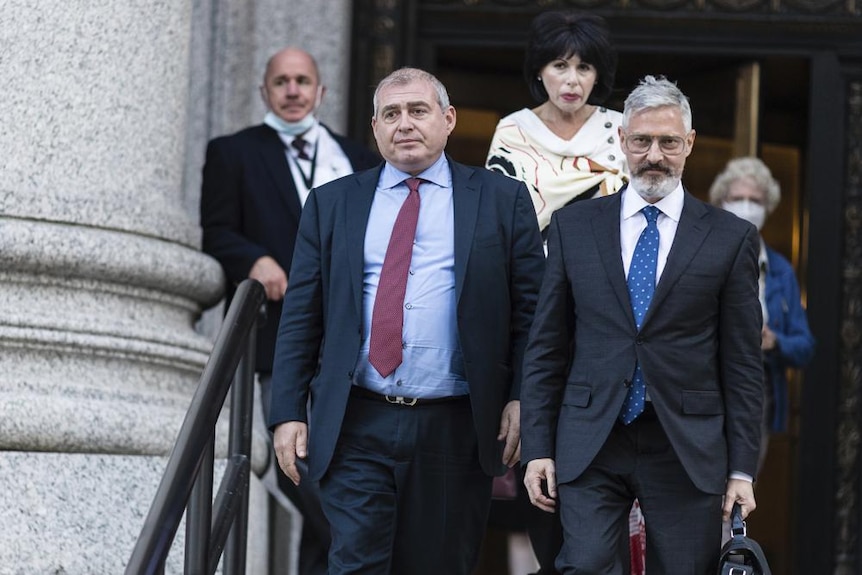 Bărbați pe scările unei instanțe de judecată în costum întunecat și cravată maro