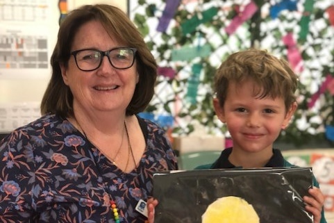 A teacher with brown hair and glasses with a young student whose scrapbook features an Aboriginal flag design.