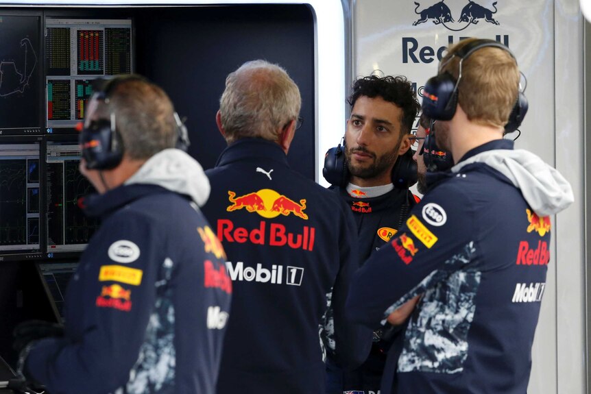Daniel Ricciardo wearing his Red Bull uniform speaking with team officials at British Grand Prix.