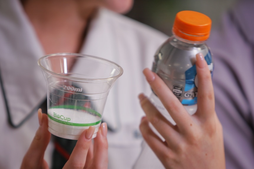 Student holding a bottle of a sports drink and a cup with sugar in it. 