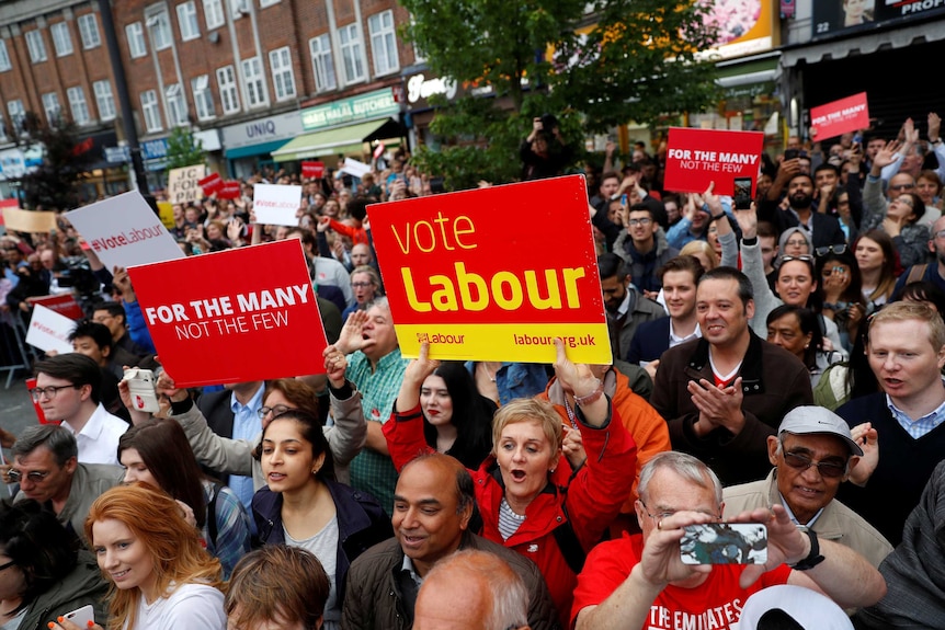 A crowd of Jeremy Corbyn supporters hold up signs at a campaign event.