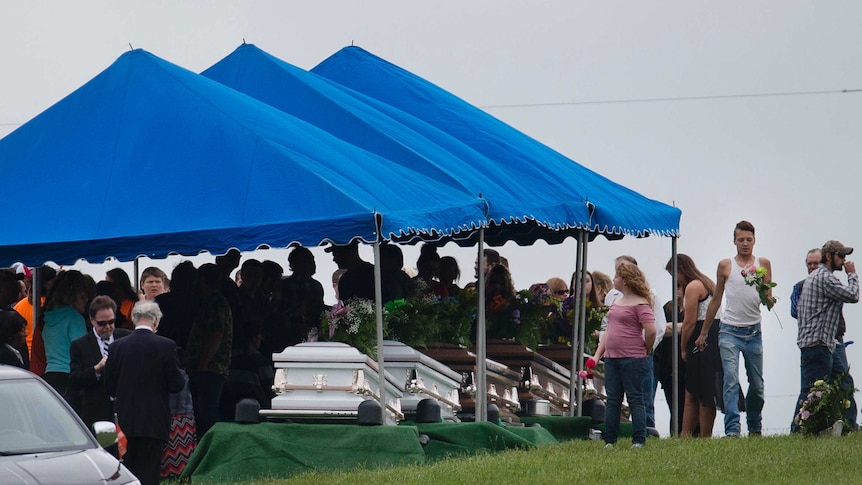 mourners gather around caskets for six of the eight members of the Rhoden family during their funeral.