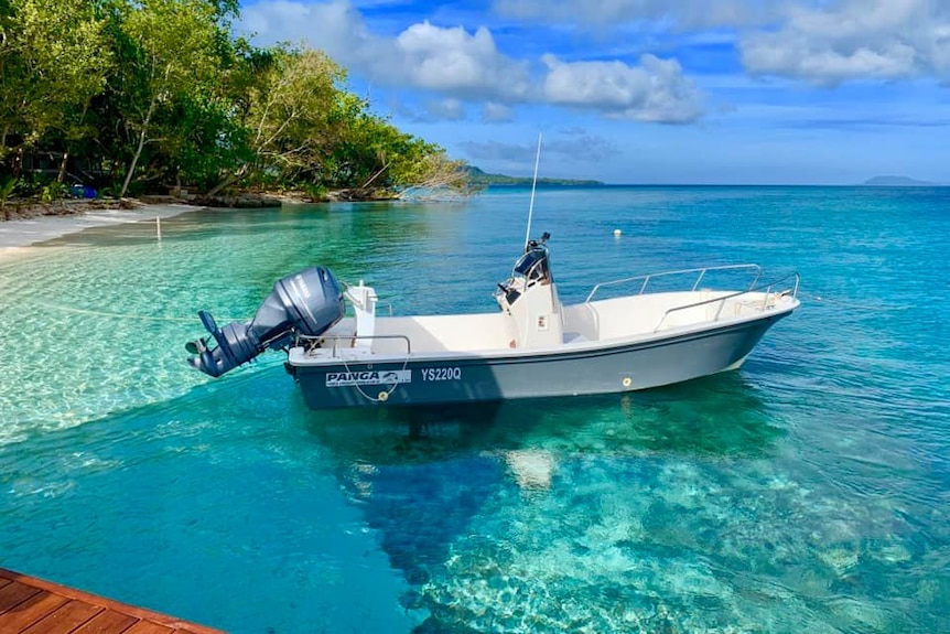 A small boat in crystal clear blue water with island in the background