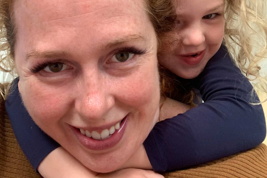 A tightly cropped image of a woman with a young child on her back. They're both smiling.