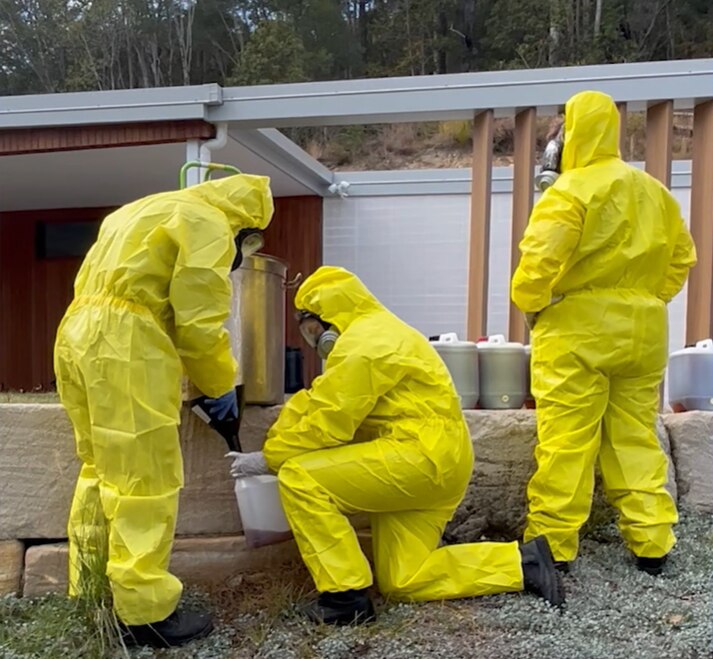 Three police officers in bright yellow hazmat suits