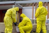 Three police officers in bright yellow hazmat suits