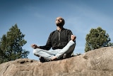Zohab Zee Khan sitting in meditation on top of a large rock depicting our 7 easy ways to start meditating.