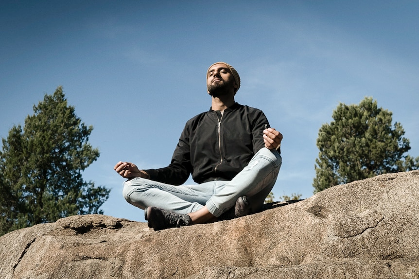 Zohab Zee Khan sitting in meditation on top of a large rock depicting our 7 easy ways to start meditating.