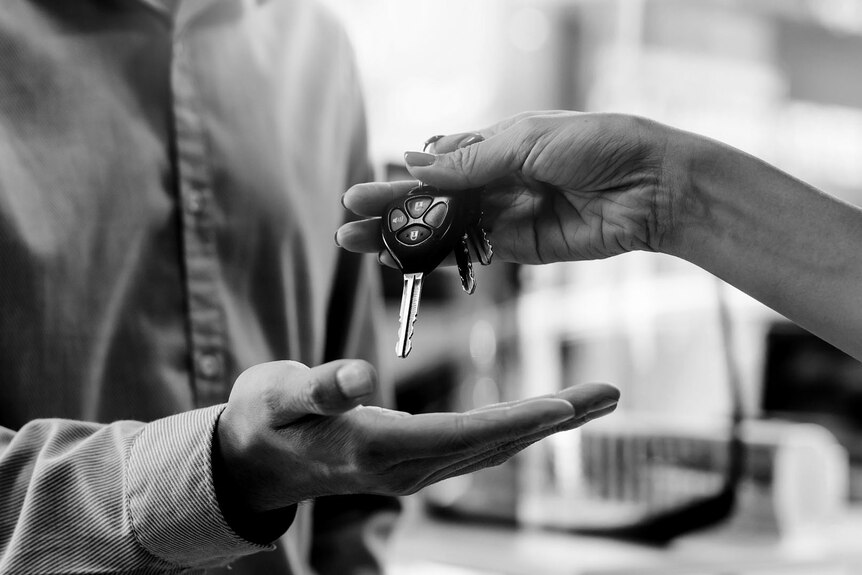 a black-and-white close-up of a woman's hand passing a set of car keys to a man