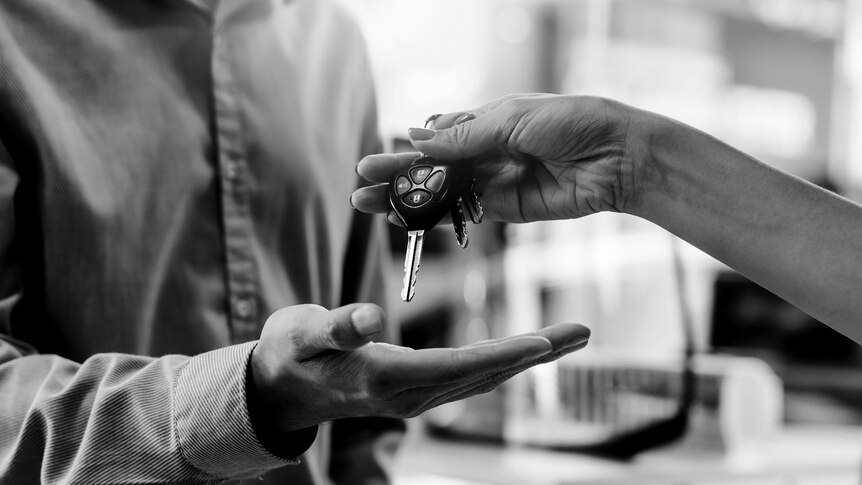 a black-and-white close-up of a woman's hand passing a set of car keys to a man
