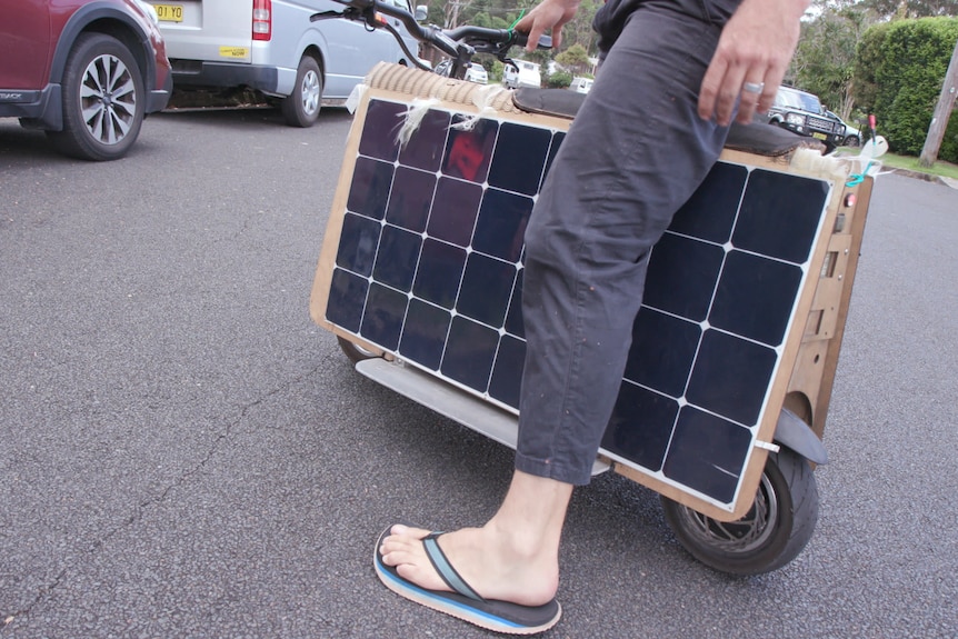 A man sits astride a scooter with solar panels as bodywork.
