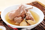 Soup with pork bones and shallots in it on a straw mat