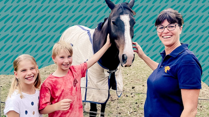 Two children and a woman from the CFS stand next to a fence patting a horse.