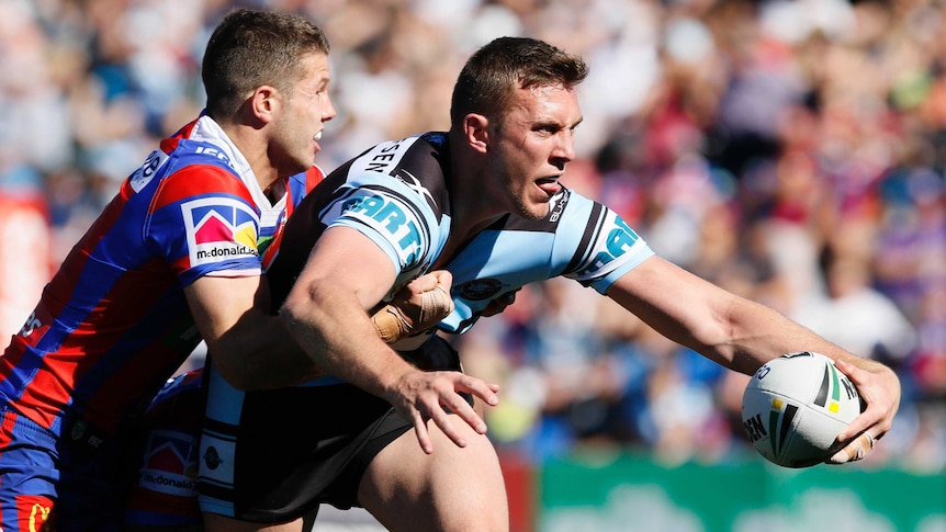Kurt Capewell looks to pass for the Sharks while being tackled by the Knights.