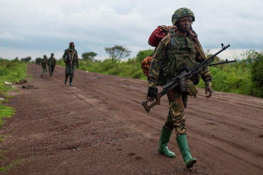 Congolese M23 rebels march down a dirt road holding weapons.