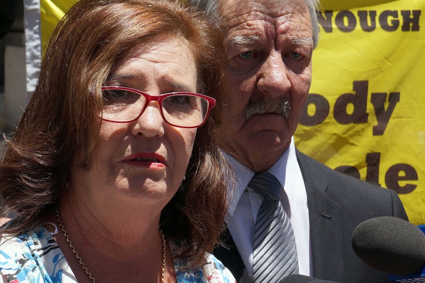 Margaret and Ray Dodd look extremely grave, in front of a sign saying 'No body, no parole'.